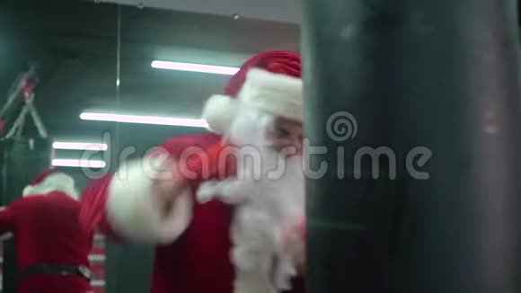 圣克劳斯拳击手与红色绷带拳击手击打一个巨大的拳击袋在拳击工作室圣诞老人拳击手视频的预览图