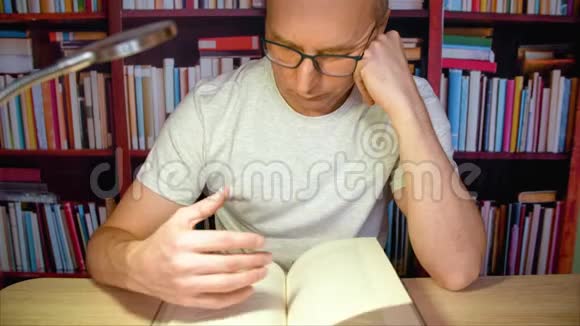 家庭客房内有书架背景的带灯的桌子上的成人阅读书籍视频的预览图