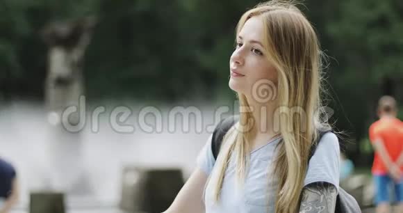 一个年轻的金发女孩骑着自行车脱下背包拿起一部手机视频的预览图