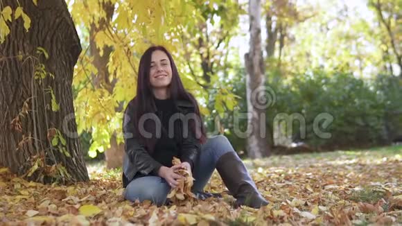 一个可爱的女孩的肖像她在秋天的公园里抛出黄色的叶子笑得很漂亮视频的预览图