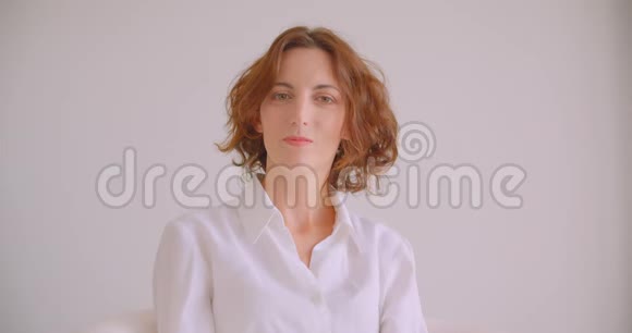 红发白种人女商人的特写镜头她看着镜头开心地坐在白色的扶手椅上视频的预览图