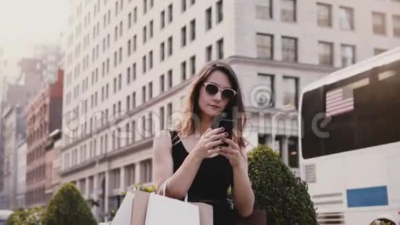 快乐迷人的高加索女商人带着购物袋在纽约的智能手机社交应用程序上和朋友聊天视频的预览图