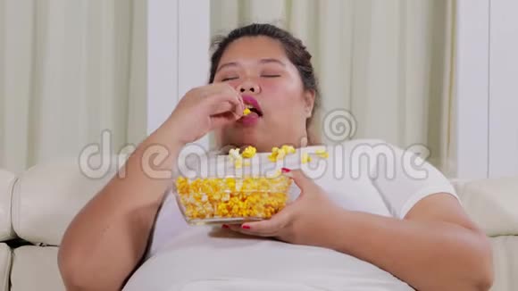 昏昏欲睡的肥胖妇女在沙发上吃爆米花视频的预览图