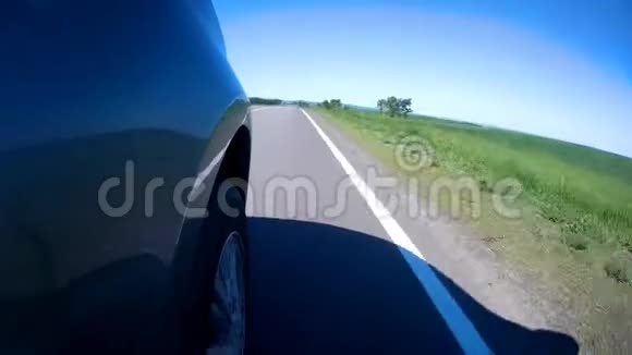 在阳光明媚的夏日沿着绿草如茵的田野在公路上驾驶一辆汽车安装在汽车侧面的照相机视频的预览图