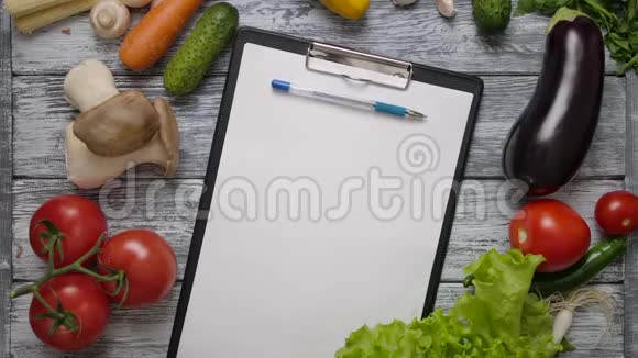 在厨房桌子上的空白剪贴板上滚动着钢笔上面有蔬菜视频的预览图