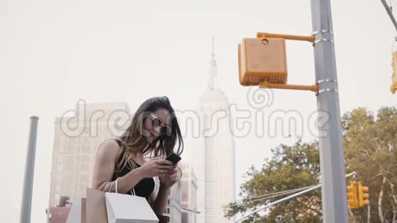 快乐美丽的白人女商人戴着太阳镜在帝国大厦附近使用智能手机应用程序购物视频的预览图