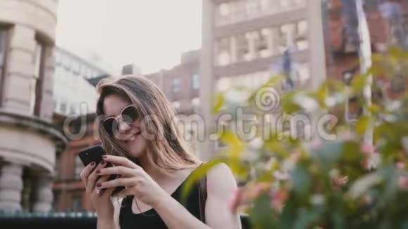快乐兴奋的白种人女性博主戴着太阳镜使用智能手机购物应用程序在纽约夏天触摸头发视频的预览图