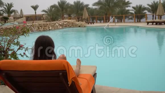 年轻的美女坐在酒店的游泳池旁的日光浴中视频的预览图