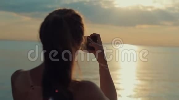 一个美丽的女孩在日落时拍了一张河的照片在智能手机上拍照视频的预览图