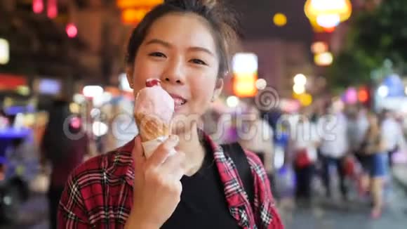 年轻有魅力的女人晚上在夜市里享用华夫饼锥里的草莓冰淇淋视频的预览图