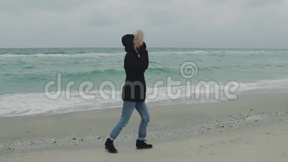 在寒冷的冬天年轻漂亮的女人在海滩上跑来跑去慢动作视频的预览图