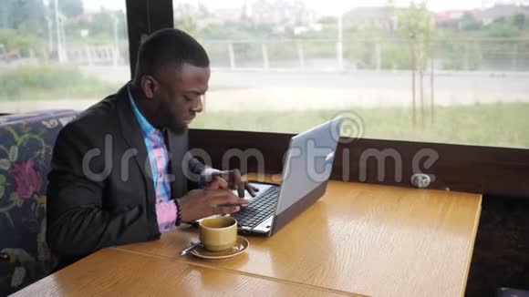 黑人商人正在夏天的咖啡馆里用笔记本电脑打字视频的预览图
