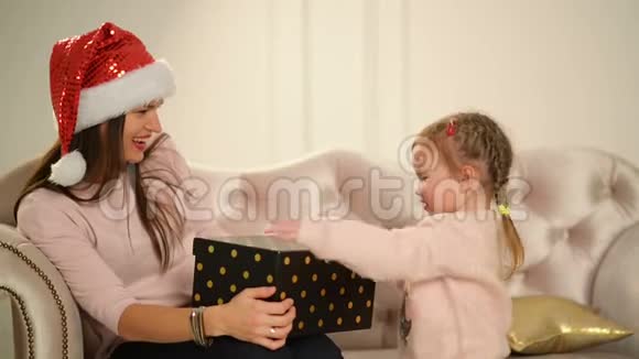 开朗的妈妈和可爱的女儿宝贝打开礼物在圣诞树附近有乐趣的父母和小孩视频的预览图