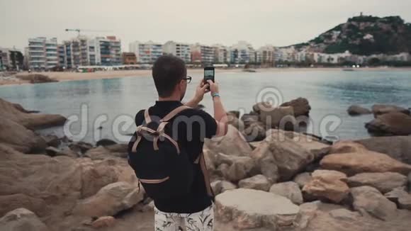 成年男子白天通过智能手机拍摄海景和城市景观视频的预览图