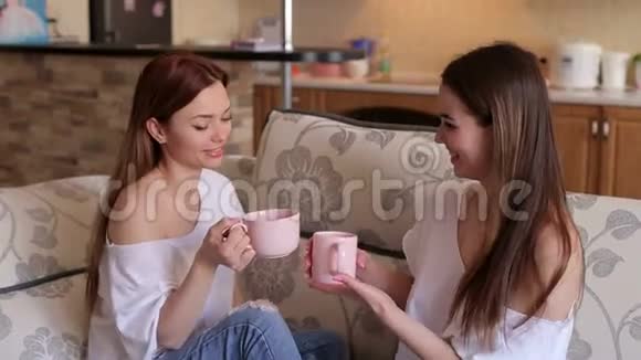 两个可爱的温柔女孩坐在沙发上喝着大杯子里的茶视频的预览图