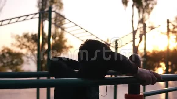 健身男在公园里做肱三头肌在双杠上的肱三头肌早上在公园里听音乐视频的预览图