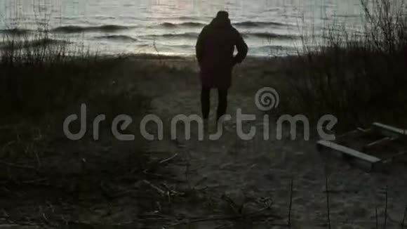 夕阳西下年轻人在海边散步孤独的男人在寒冷的日子独自在海滩上度过视频的预览图