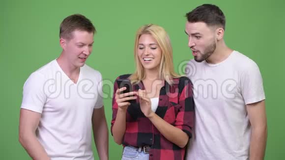 三个快乐的年轻朋友一起用电话获得好消息视频的预览图
