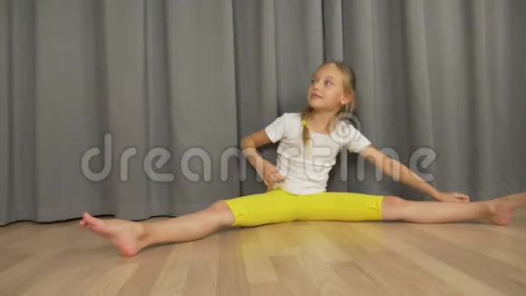 小女孩在室内起居室里做劈腿和伸展运动快乐的小女孩坐着跳舞视频的预览图