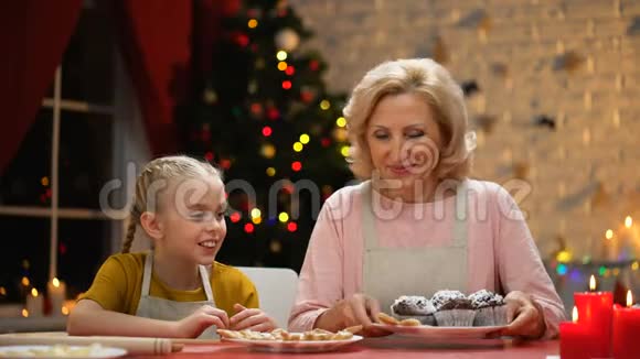 可爱的女孩吹着松饼上的糖粉奶奶微笑着家庭圣诞时光视频的预览图