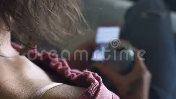 年轻女孩躺在沙发上拿着啤酒罐和智能手机久坐不动的生活方式视频的预览图