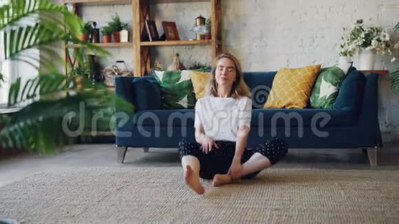 漂亮的年轻女子在家练习瑜伽以简单的身体姿势放松坐在地板上带着漂亮的家具视频的预览图