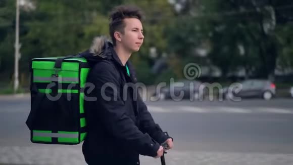 送货员带着绿色背包骑着滑板车穿过城市带着食物送货视频的预览图