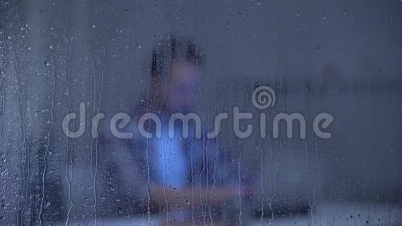 专注的中年男子在雨窗后的笔记本电脑上工作自由职业者视频的预览图