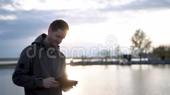 这家伙正在用平板电脑或触摸屏邮寄湖上的游客和太阳灯视频的预览图