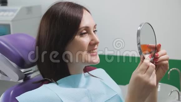 治疗后坐在牙科椅上的年轻女子在镜子里检查她的牙齿牙齿护理概念视频的预览图