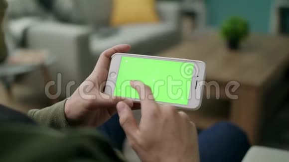 一个男人在智能手机上选择一个角色客厅里有一个绿色的屏幕视频的预览图