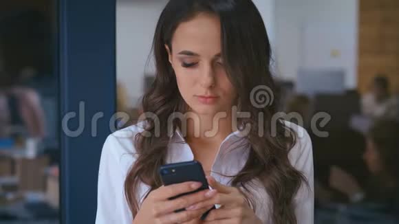 一位年轻漂亮的商务女性后台办公室里有智能手机发短信视频的预览图