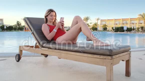 性感的女孩用手机在游泳池附近放松女人躺在手机上发短信上网视频的预览图