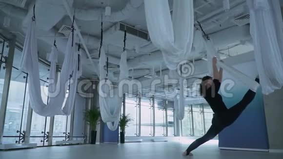 有魅力的女人用瑜伽吊床在健身中心伸展她的腿有大的地板到天花板的窗户许多视频的预览图