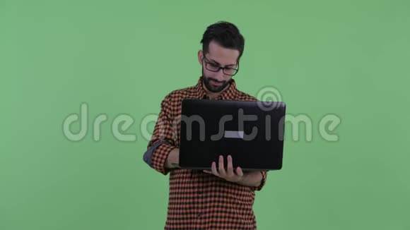 快乐年轻的留着胡须的波斯时髦男人一边用笔记本电脑一边思考视频的预览图