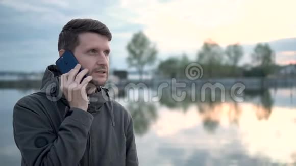 年轻人在湖边的森林里打电话他有一个自然假期视频的预览图