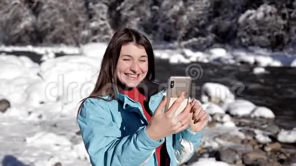 冬天森林里靠近山河的女孩用手机在视频上聊天视频的预览图