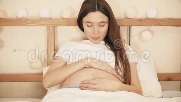 美丽的孕妇在床上抚摸她的腹部视频的预览图