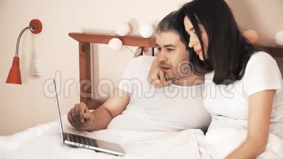 快乐的一对情侣在床上用笔记本电脑在网上购物视频的预览图