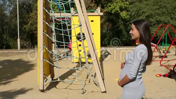 年轻的孕妇在游乐场附近的公园里散步视频的预览图
