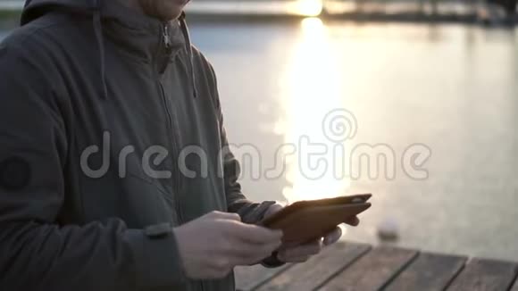 男人正在美丽的日落背景上的平板电脑上打字快关门视频的预览图
