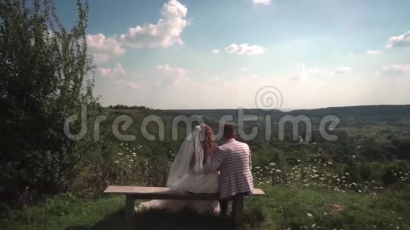 浪漫的新婚夫妇坐在自然的长凳上在教堂里观看视频的预览图