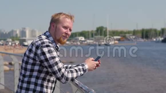 一个年轻的金发男人拿着电话站在水边男人正在打电话留言年轻的学生走过视频的预览图