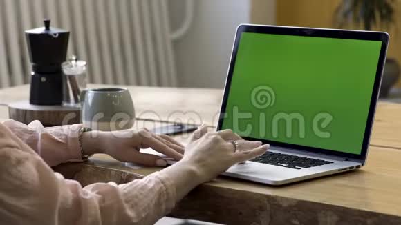 用手提电脑用绿色屏幕站在现代的桌子上用手指上戴着一枚金戒指的女性双手合上视频的预览图