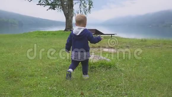 小男孩走在山湖附近在大自然中奔跑嬉戏慢动作视频的预览图