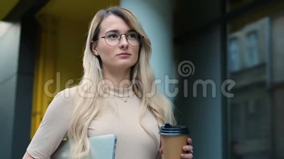 一位年轻漂亮的商业女性的肖像戴着眼镜的学生在城市里走来走去喝着咖啡去视频的预览图