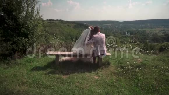 浪漫的新婚夫妇坐在长凳上看着教堂视频的预览图