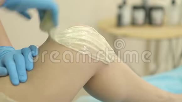水疗沙龙的脱毛蜡美容师给妇女的腿上蜡特写镜头视频的预览图