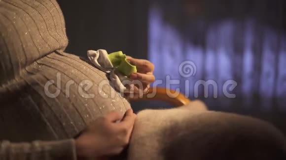 不明身份的孕妇坐在黑暗的房间里的摇椅上抚摸着肚子玩着一只小袜子视频的预览图