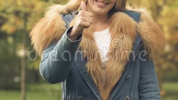 穿着秋装的女人带着毛皮竖起大拇指宣传温暖的衣服视频的预览图